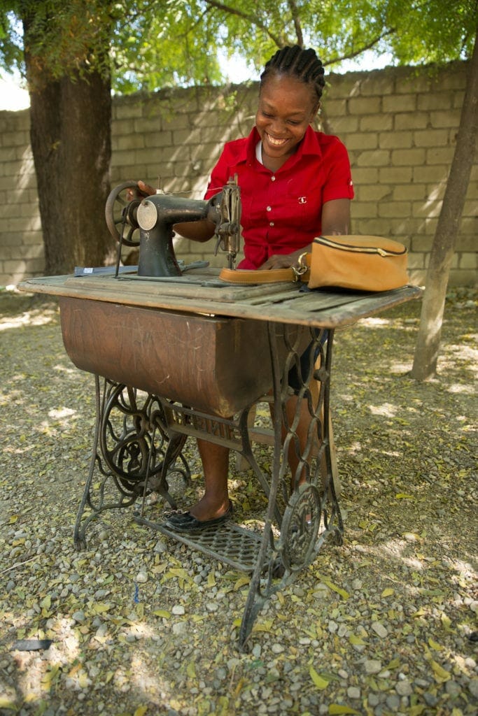 A worker smiles at her sewing machine as she creates custom leather goods