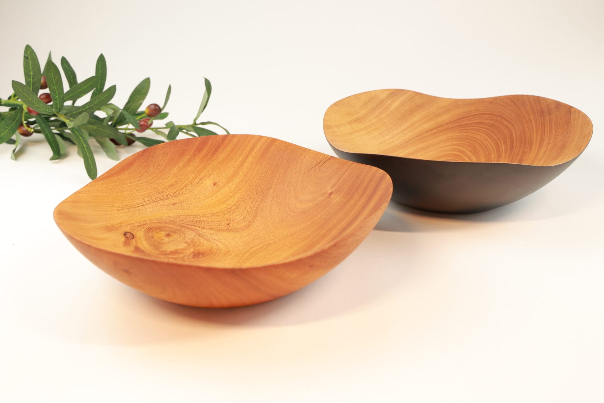 Itza Wood wave bowls in regular and char charred and regular wooden wave bowls next to each other and seated next to holly leaves