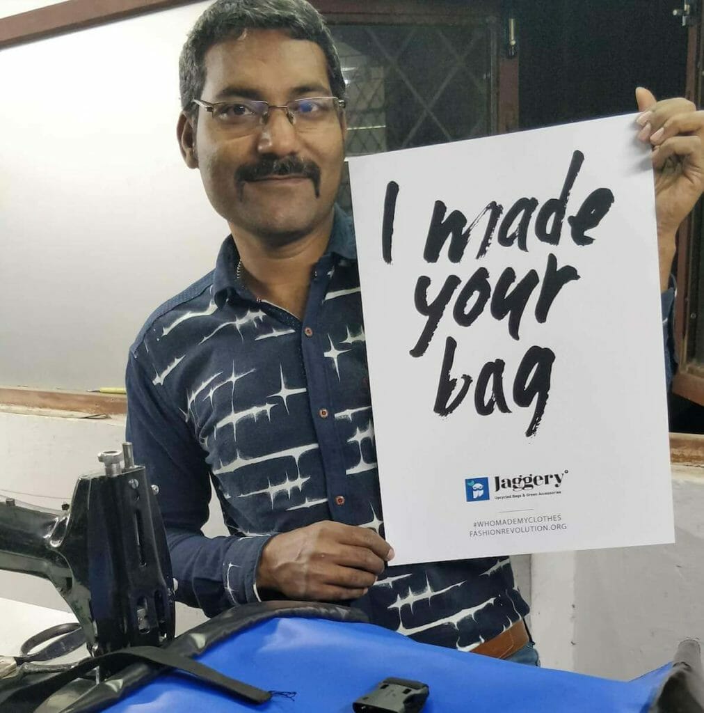 A worker at Jaggery holds up a sign that says "I made your bag." He is just one of the employees who create fair trade, high quality branded logo bags.