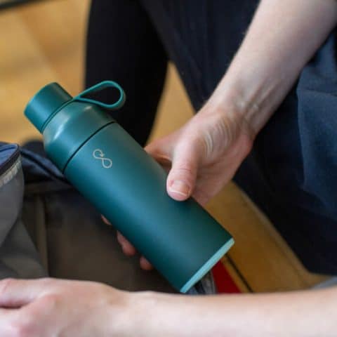 Custom water bottle with logo, shown with a hand taking it from a backpack pouch