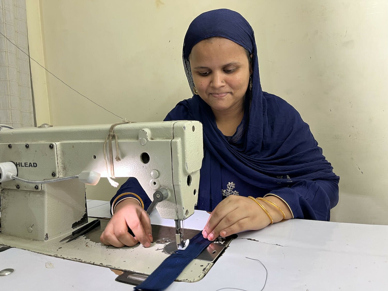 Farida sits at a sewing machine, working on Levi's customer giveaway keychains