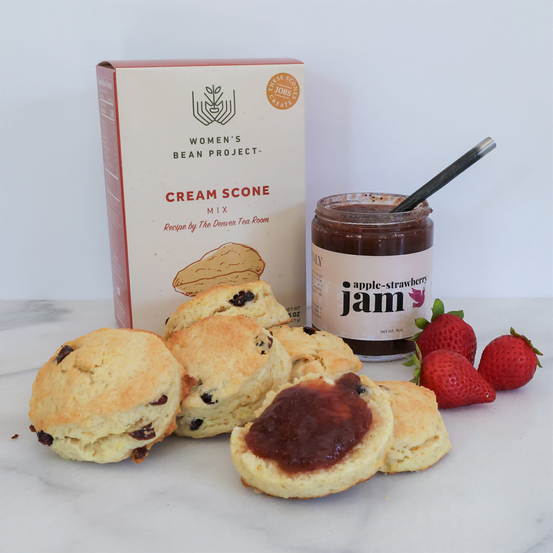 The scones and jam gift basket includes scone mix and apple strawberry jam. The photo shows baked scones with jam and fresh strawberries.