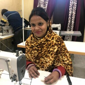 A worker sits at a sewing machine, smiling