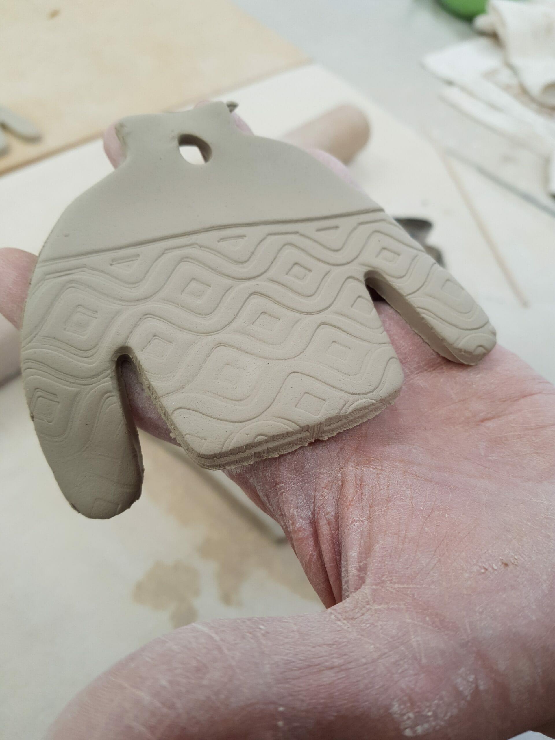 A hand holds an ugly sweater ornament before it's glazed and fired