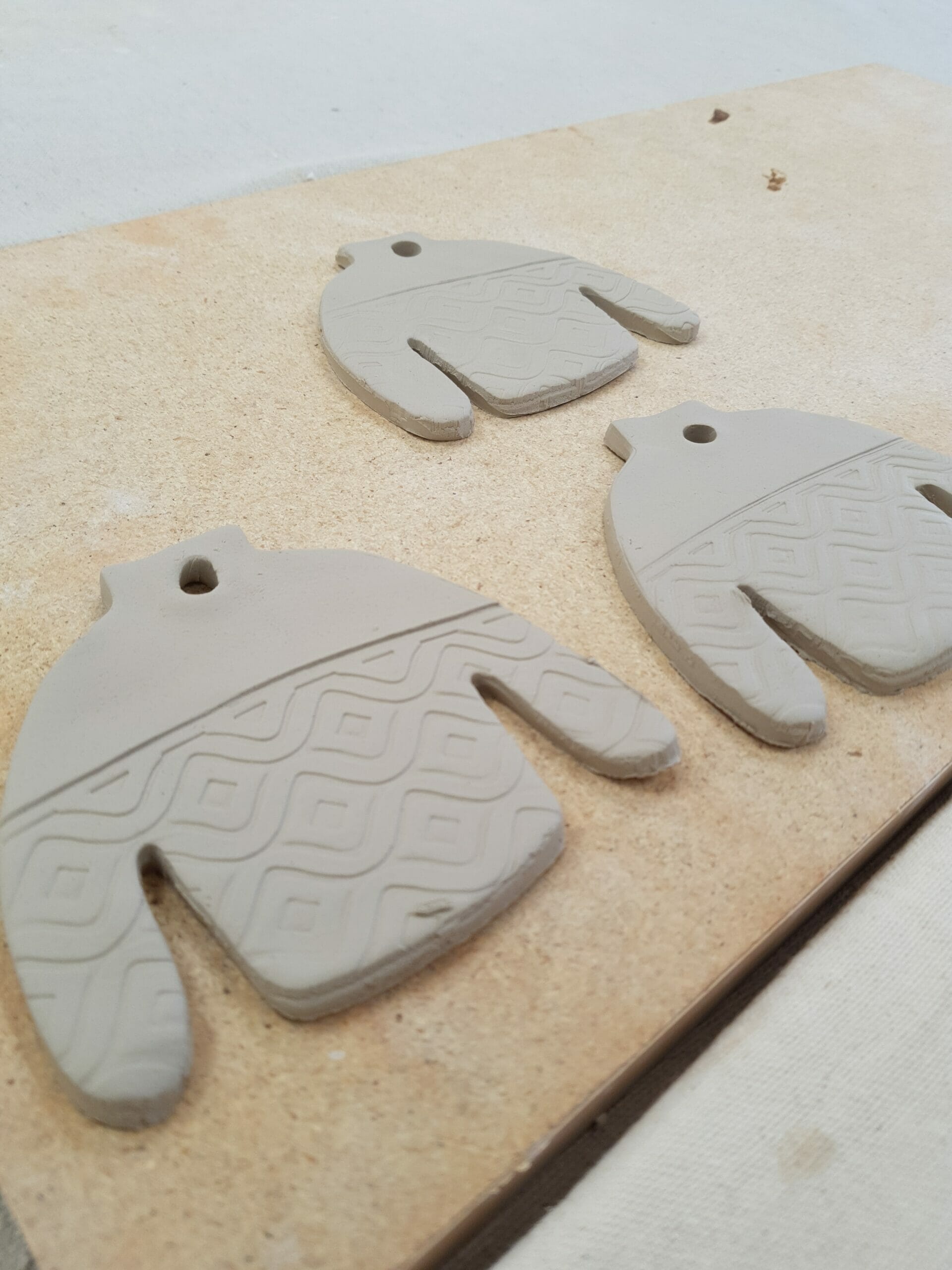Three ugly sweater ornaments lie on a table before being glazed and fired