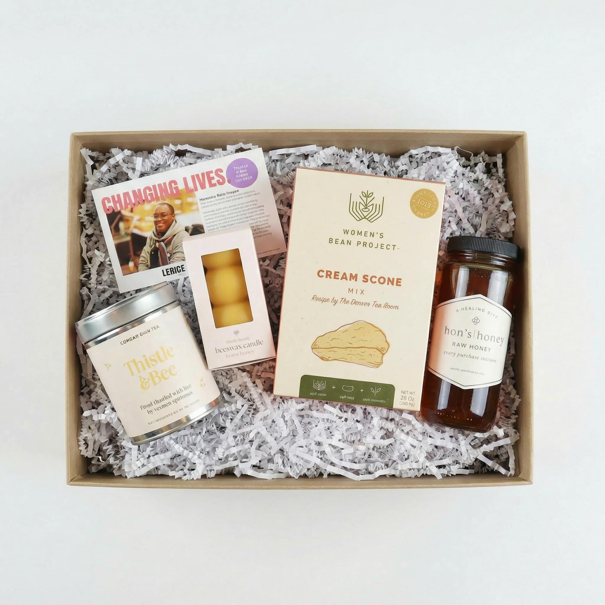 comfort and care white background a birds eye view of a gift set featuring tea, scone mix, honey, and a candle made from honey along with an impact card telling about the makers