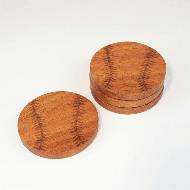 one coaster engraved to look like a baseball sits next to a stack of three of the same coaster