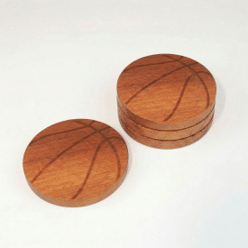 one coaster engraved to look like a basketball sits next to a stack of three of the same coaster