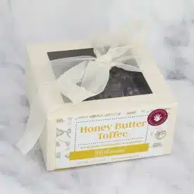 Rethreaded 1lb box toffee A box of Honey Butter Toffee with a white bow wrapped around it sits on a marble countertop